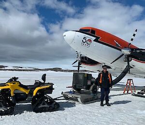 A man standing in front of a red and white twin propeller aircraft on the sea-ice