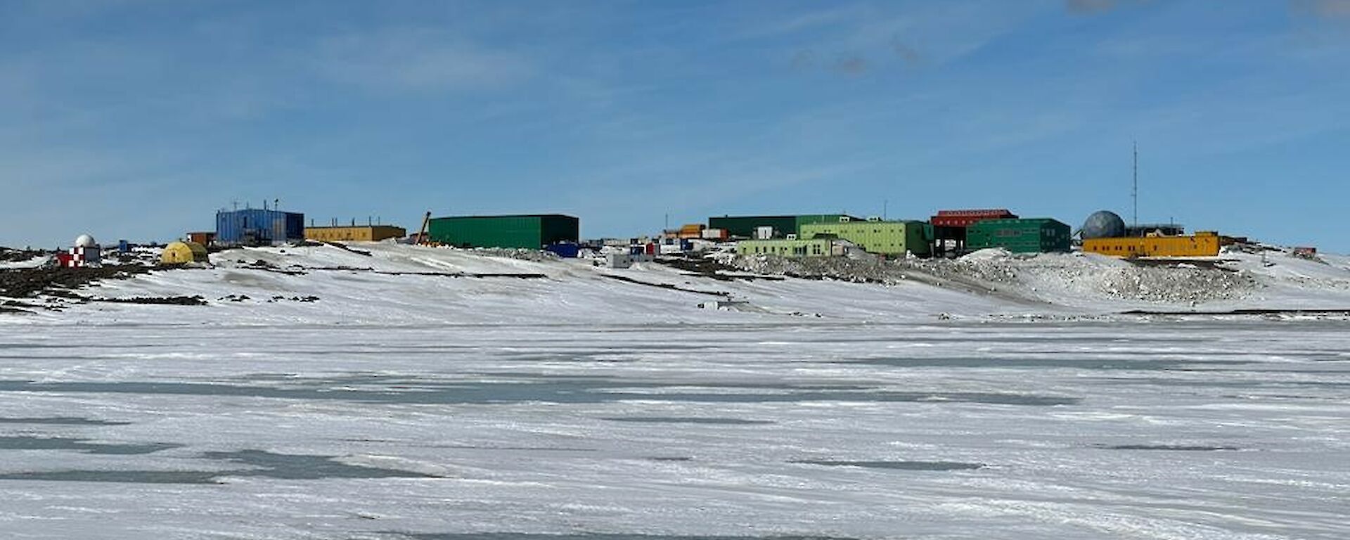 Many colourful buildings sitting amongst hills in an icy snow-covered landscape with sea-ice in the foreground