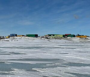 Many colourful buildings sitting amongst hills in an icy snow-covered landscape with sea-ice in the foreground