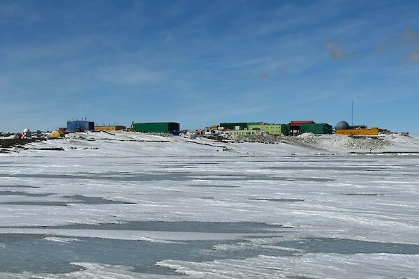 Many colourful buildings sitting amongst hills in an icy snow-covered landscape with sea-ice in the foreground