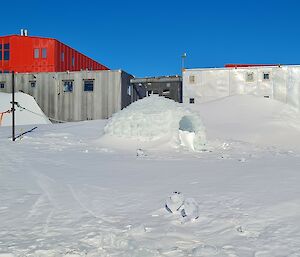 Igloo shines in the sunshine, with station buildings behind and blue sky above