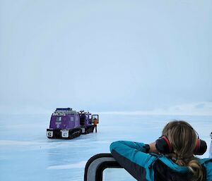 Purple snow vehicle on ice with person watching in foreground