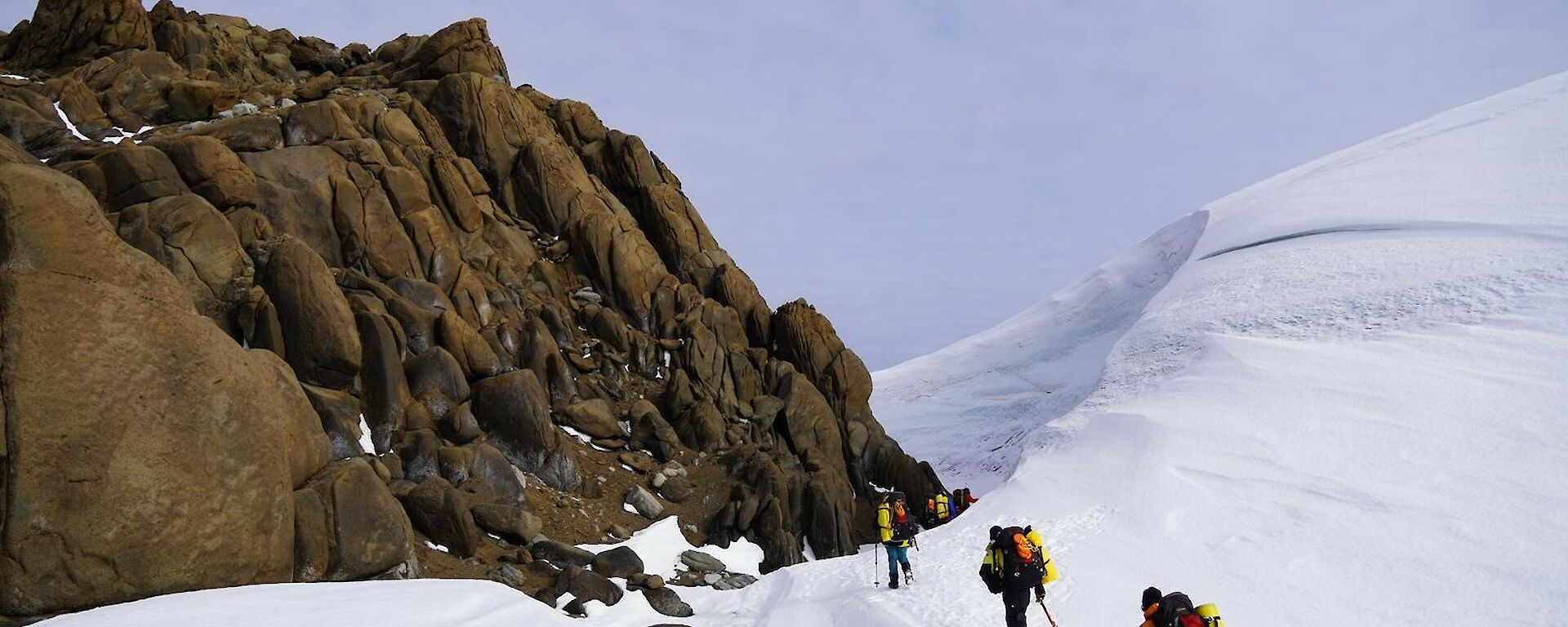 People walking to a rock outcrop past a snow cornice