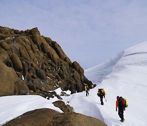 People walking to a rock outcrop past a snow cornice