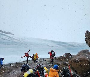 Group of expeditioners on rocks in snowfall with an ice wall behind them
