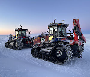 Two tractors parked on a snowy plain under a dim sky with a sunset or sunrise glow on the horizon.