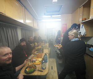 A group of expeditioners sit at a long table in a small room.