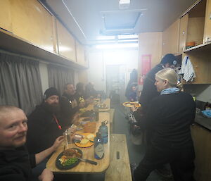 A group of expeditioners sit at a long table in a small room.