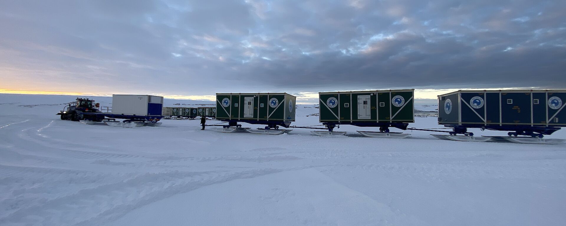 A series of rectangular cabins mounted on skis, hitched together to be towed by tractor across the snow.