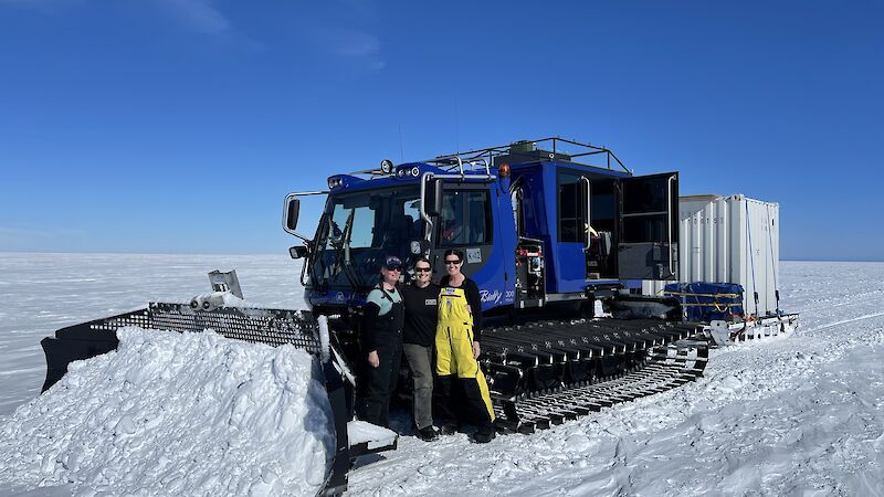 Expeditioners pose with a blue vehicle that has been pushing snow.