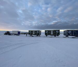 A series of rectangular cabins mounted on skis, hitched together to be towed by tractor across the snow.
