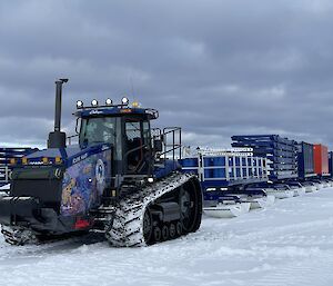 A tractor tows a train of containers on sleds across the ice.
