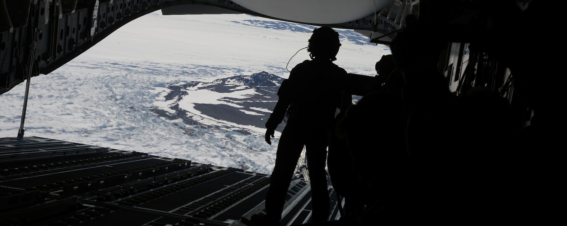 A silhouette of a person facing the back of an open c17a aircraft before an airdrop