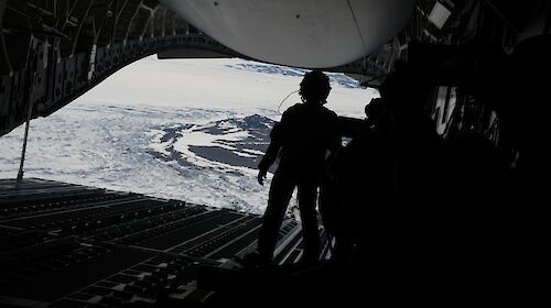 A silhouette of a person facing the back of an open c17a aircraft before an airdrop