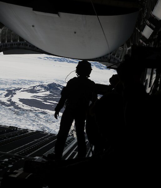 A silhouette of a person facing the back of an open c17a aircraft before an airdrop