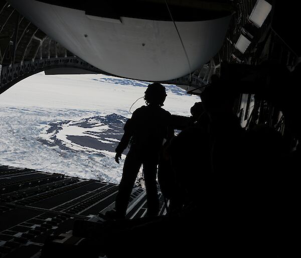 A silhouette of a person facing the back of an open c17a aircraft before an airdrop