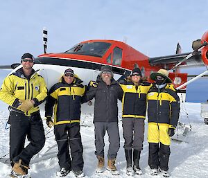 Five people stand in front of a red plane in Antarctica