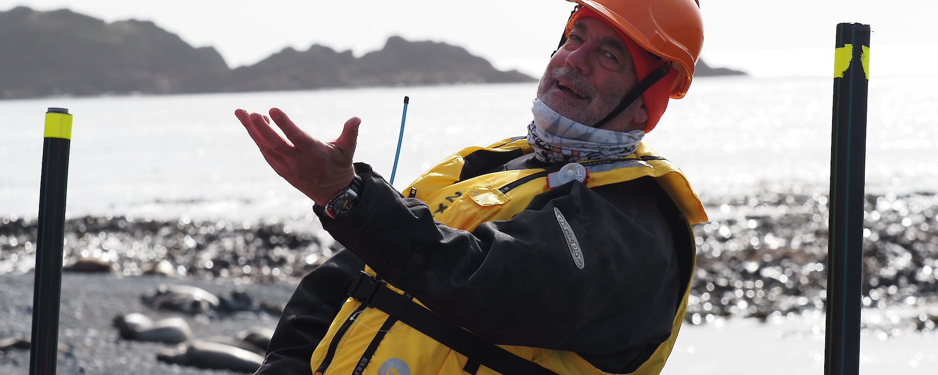 A man in a life jacket makes a dramatic gesture with his hand