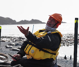 A man in a life jacket makes a dramatic gesture with his hand