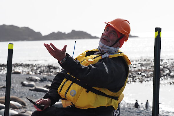 A man in a life jacket makes a dramatic gesture with his hand