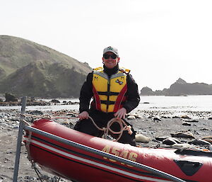 A man in a lifejacket sitting in a boat parked on a rocky beach
