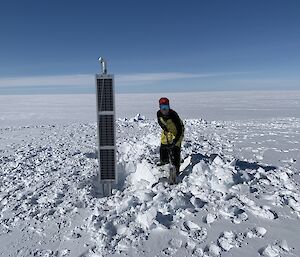 Geophysicist Anya Reading smiling whilst digging snow to anchor a solar panel attached to a seismometer.