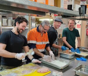 Four people smiling whilst crumbing chicken fillets at Casey kitchen