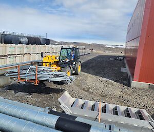 A man inside a yellow vehicle that is lifting a large pile of steel piping