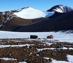 A field hut with a hagglunds vehicle and mountains rising behind