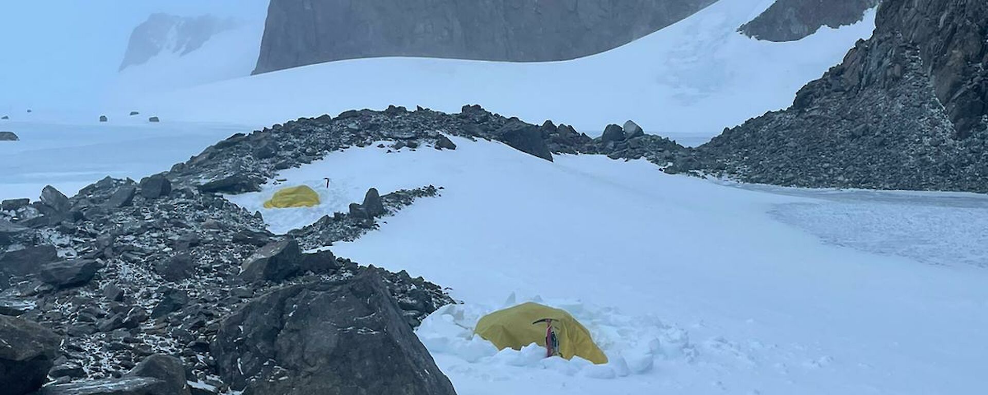 An expeditioner inside a yellow survival bivvie surrounded by snow and rocks