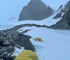 An expeditioner inside a yellow survival bivvie surrounded by snow and rocks