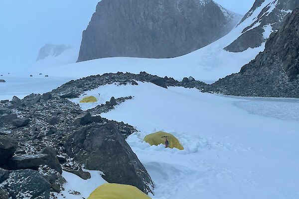 An expeditioner inside a yellow survival bivvie surrounded by snow and rocks