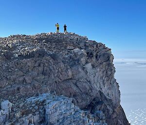 Two people standing near the edge of a cliff and the vast antarctic landscape behind them