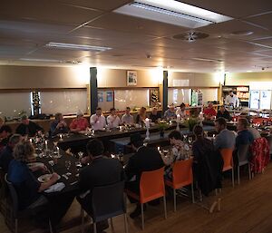 30 well-dressed people sitting around a candlelit table eating their Christmas meal