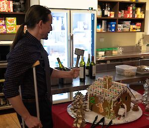 A smiling man with a meat tenderiser is about to break open a Christmas Gingerbread House