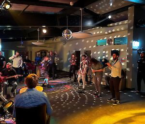 A group of people under colourful disco lights dancing to a band playing music