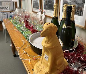 A small plastic guide dog sits on a bench with Christmas decorations and some champagne