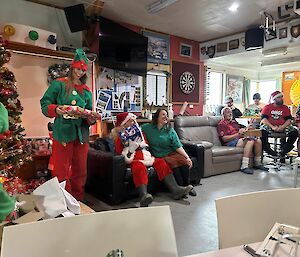 A group of people in Christmas outfits sit in a lounge room