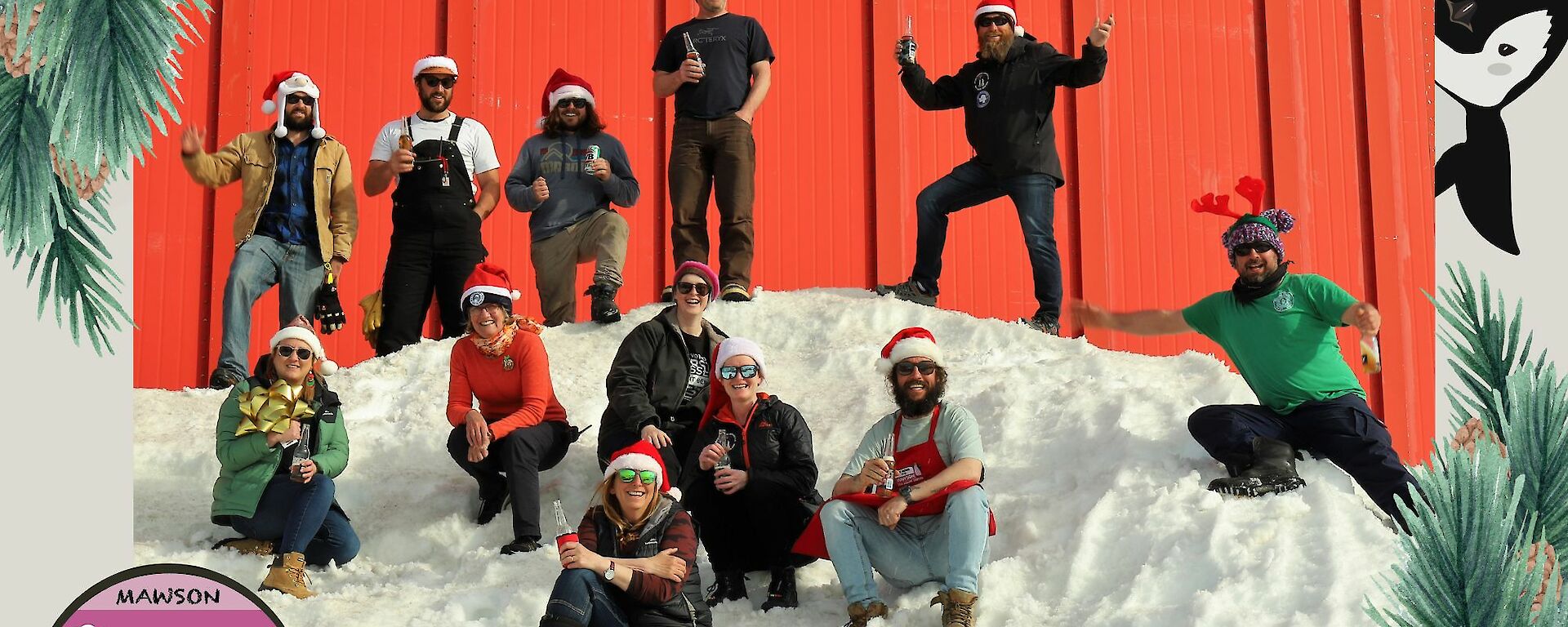 Small team on snow in front of red workshop building smiling at camera wearing Santa caps or reindeer horns, photo surrounded by Christmas message and Mawson crest