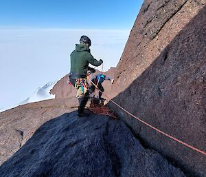 Looking down rocky slope and two men climbing up, attached via ropes and harnesses