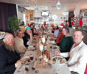 Long table set for Christmas with 12 people sitting and smiling to camera