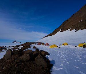 Camp site with yellow and red tents, looking back across ice plateau to another mountain range