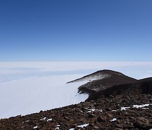 Undulating rocky slope down to ice plateau with two Hägglunds seen way in the distance at bottom