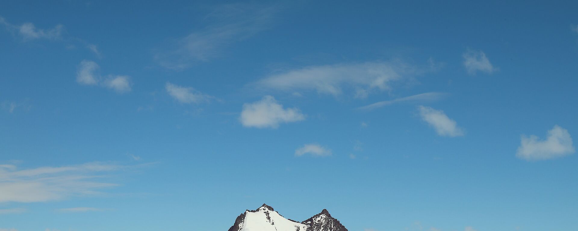 Rocky peak rises out of the ice plateau, blue skies above