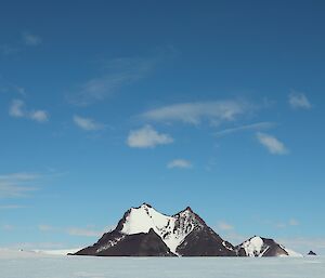 Rocky peak rises out of the ice plateau, blue skies above