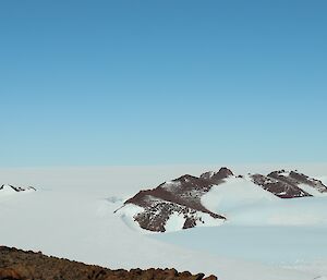 Man on peak in foreground, looks out across ice plateau to mountain range in the distance