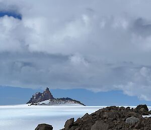 An ice plateau reaches to mountain range with one distinct pointy mountain peak, cloudy grey sky above