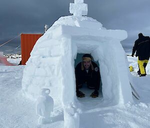 Antarctic expeditioner crouched inside a small igloo