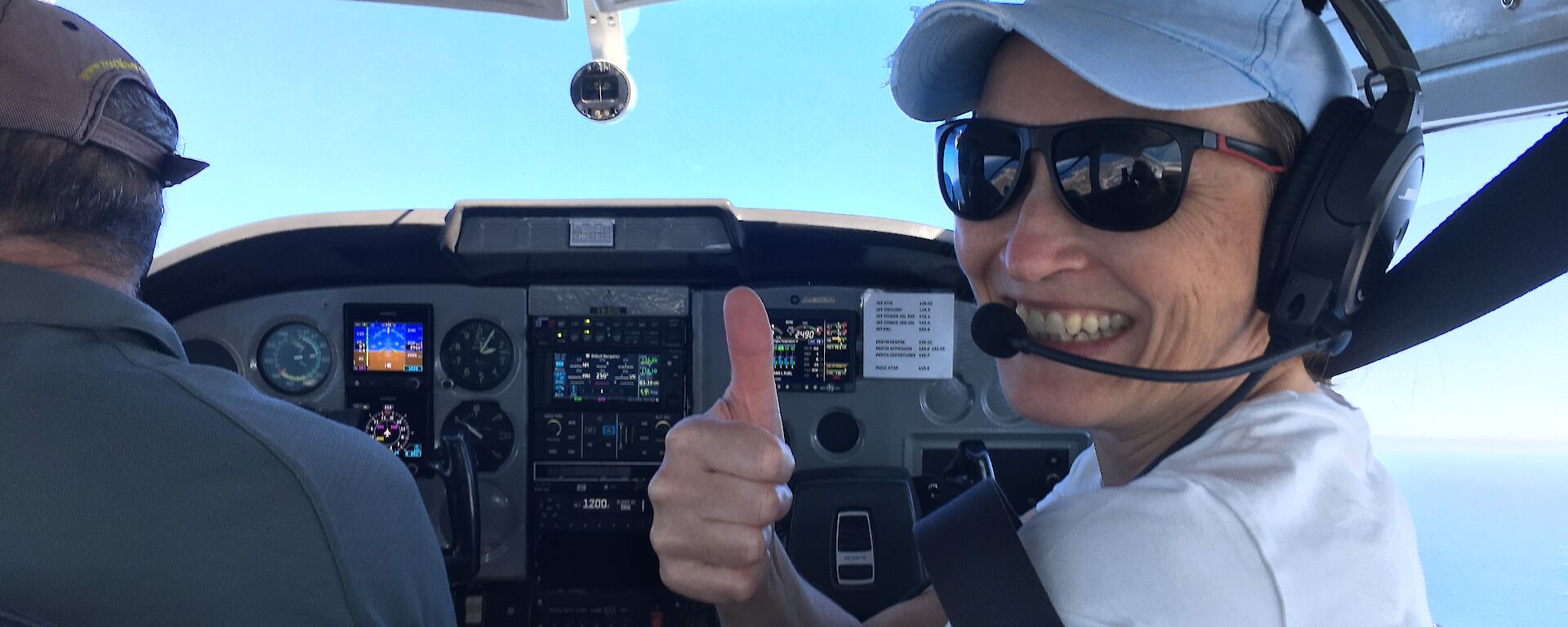 A woman smiles from the cockpit of a small plane