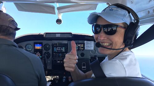 A woman smiles from the cockpit of a small plane